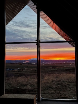 A room with a large window offering a view of a sunset over a mountainous landscape.
