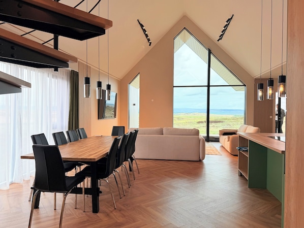 A modern interior with a dining area, sofa, and large windows offering a view.