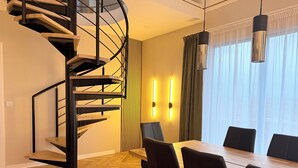 Een modern interieur met een wenteltrap, een eethoek met een houten tafel en stoelen, en een groot raam met gordijnen.