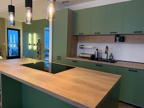 A modern kitchen with green cabinets, a wooden countertop, and pendant lights.