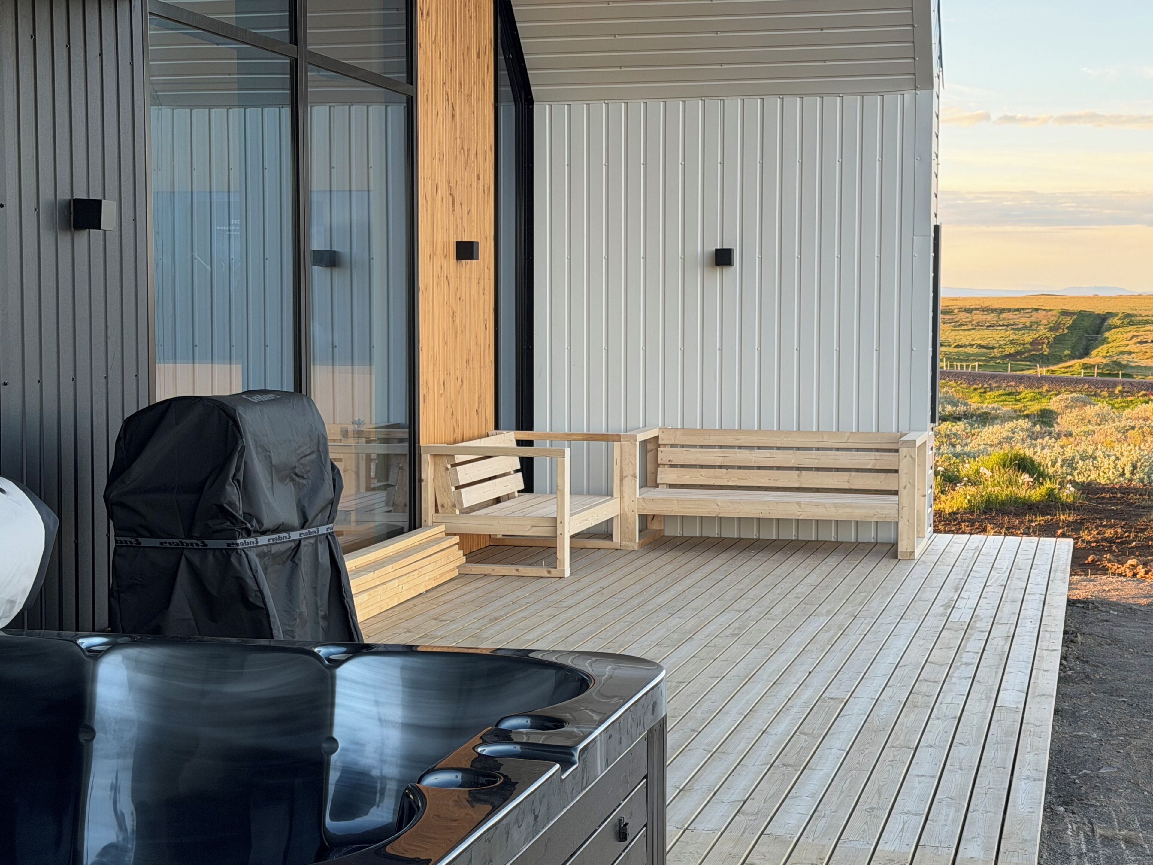 A modern outdoor deck with a wooden bench, a grill, and a hot tub.