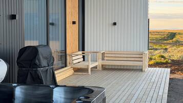 A modern outdoor deck with a wooden bench, a grill, and a hot tub.