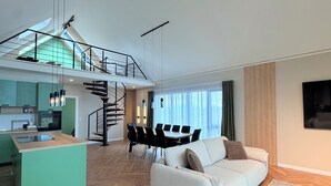 Een ruime woonkamer met een bank, een eettafel en een keuken op de achtergrond.