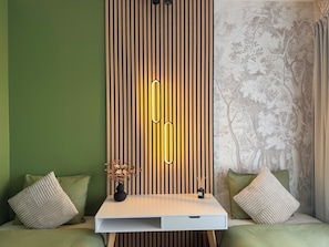 A room with a white desk, a vertical wooden panel with a light fixture, green walls, and a patterned wallpaper.