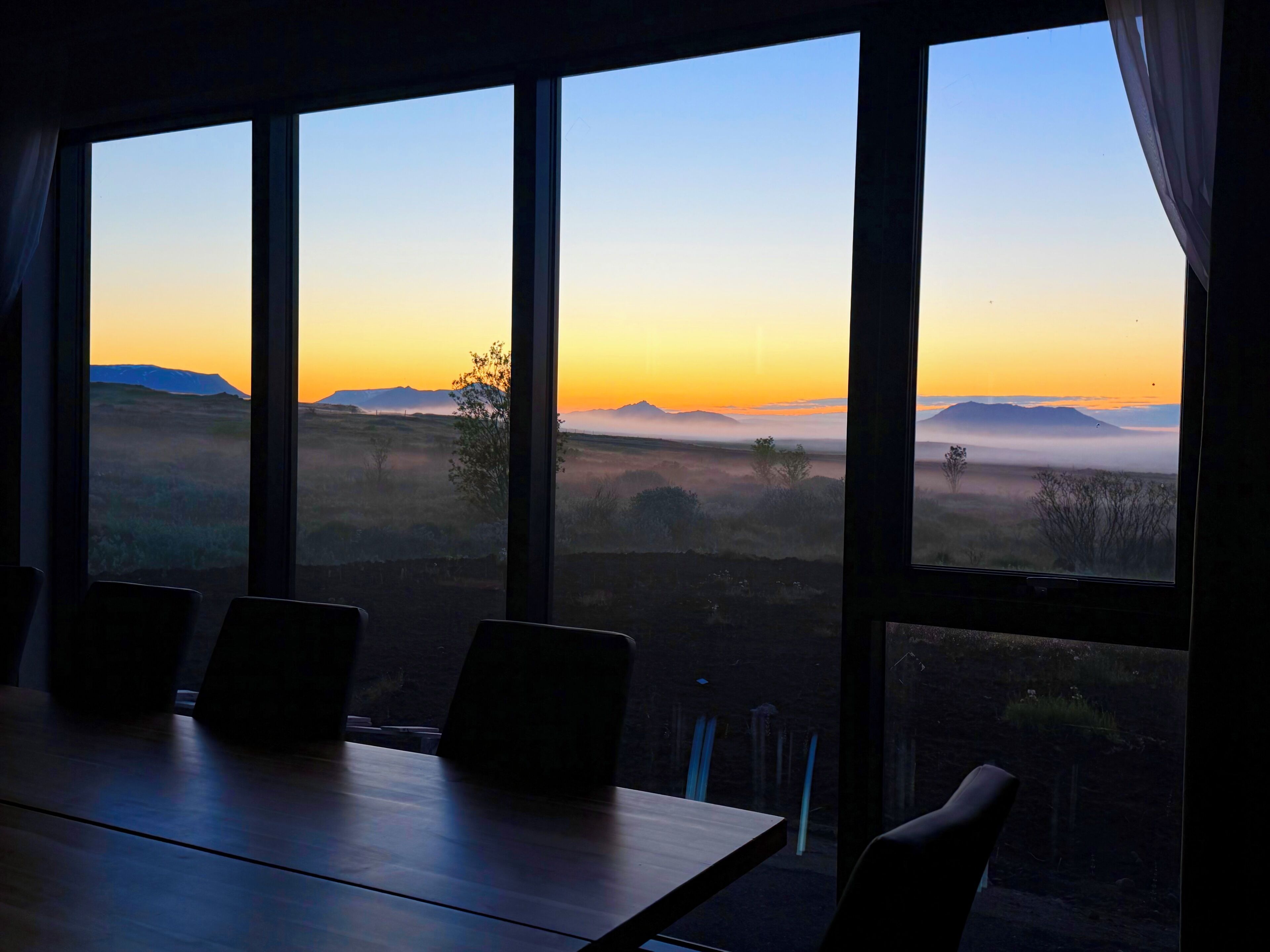 Una sala conferenze con un tavolo grande e sedie, affacciata su un paesaggio con montagne e cielo sereno.