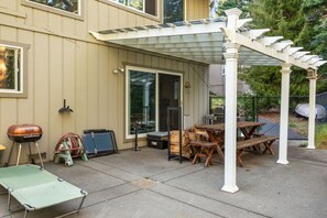 A covered patio with a pergola, a barbecue grill, a folding chair, and a table.