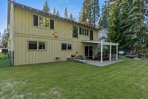 A two-story house with a covered patio area, a fenced yard, and a view of tall trees.