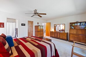 A bedroom with a bed, a ceiling fan, wooden furniture, and a mirror.