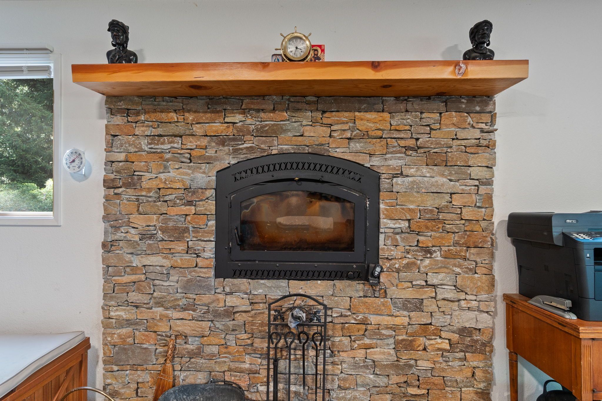 Una chimenea de piedra con un reloj encima, un repisa de madera y una impresora en un escritorio a la derecha.