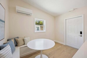 Ein Zimmer mit Klimaanlage, einem kleinen Fenster mit Blick auf Grünflächen, einer weißen Tür und einem weißen runden Tisch.