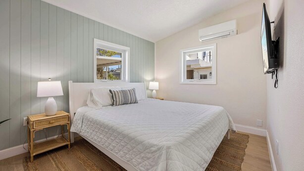 Un dormitorio con una cama, dos mesitas de noche, una ventana y un televisor instalado en la pared.