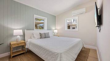 Une chambre à coucher avec un lit, deux tables de chevet, une fenêtre et un téléviseur fixé au mur.