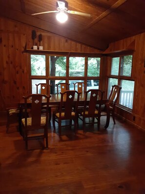 A wooden dining room with a table and chairs, large windows, and a ceiling fan.