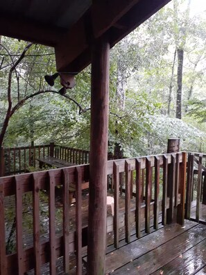 Una terraza de madera con barandilla, rodeada de árboles.