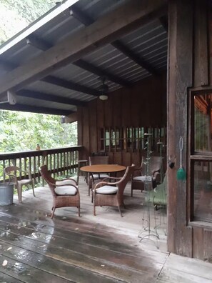 Una terraza de madera con una mesa, sillas, barandilla y una puerta con un adorno colgante.