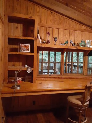 Un bureau en bois, une lampe, une chaise et une fenêtre donnant sur des arbres.