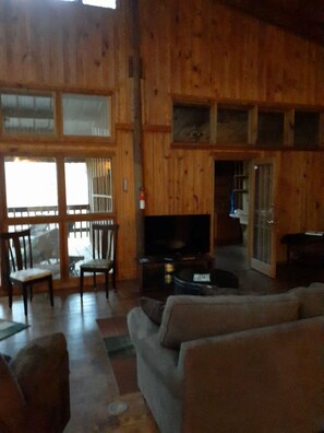 Un intérieur en bois comprenant un canapé, des fauteuils, un téléviseur et une porte-fenêtre coulissante donnant sur un espace extérieur.
