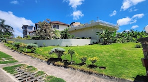 A residential property with a paved driveway, a grassy lawn, and a white fence.