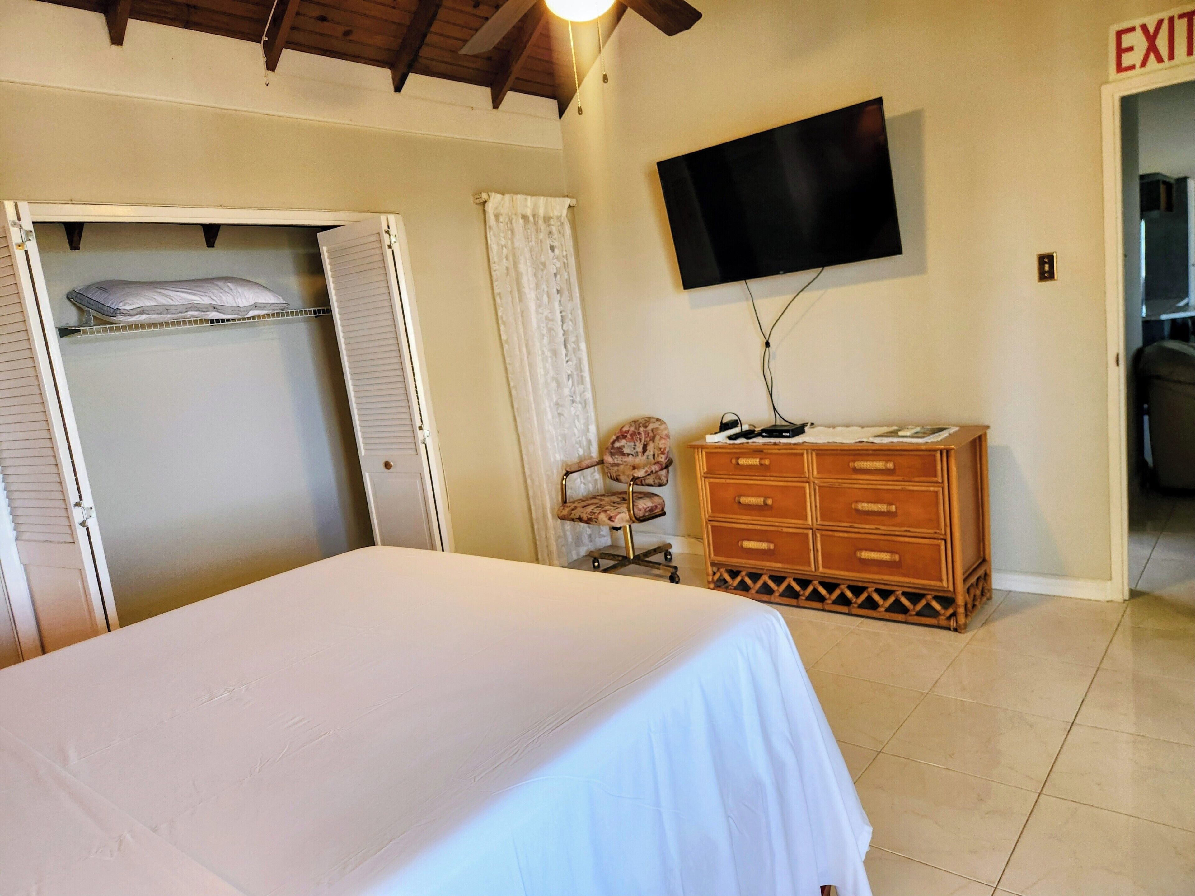 A bedroom with a bed, a dresser, a television, and an exit sign.