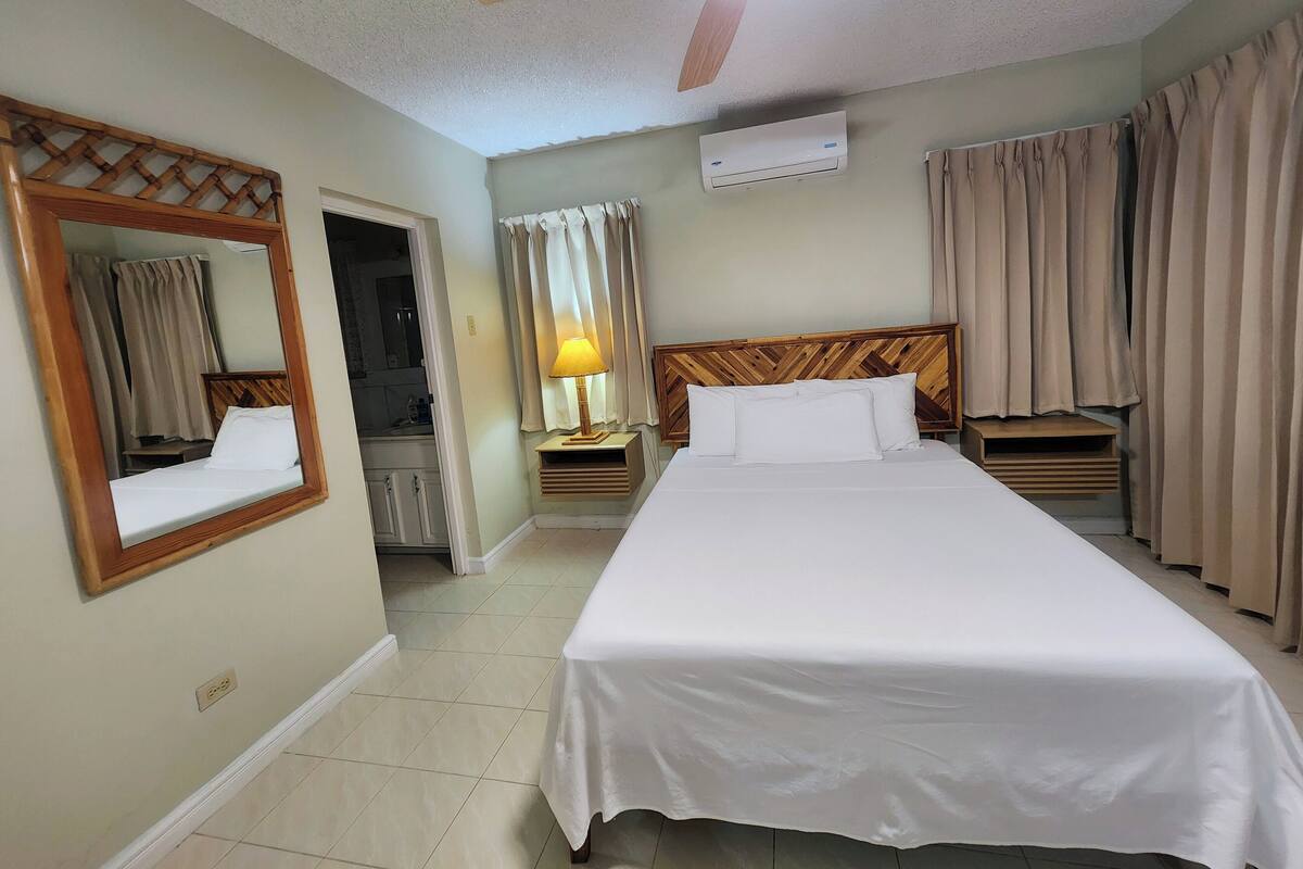 Une chambre d’hôtel équipée d’un lit, d’un ventilateur de plafond, d’un appareil de climatisation, d’un miroir et de rideaux.
