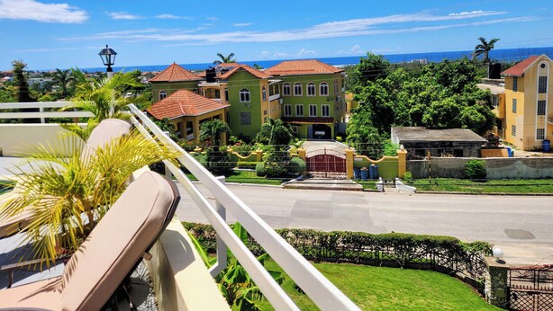 A residential area with multiple houses, a well-maintained lawn, and a clear view of the ocean. - Comfy Villa With Ocean View (St. James Parish)