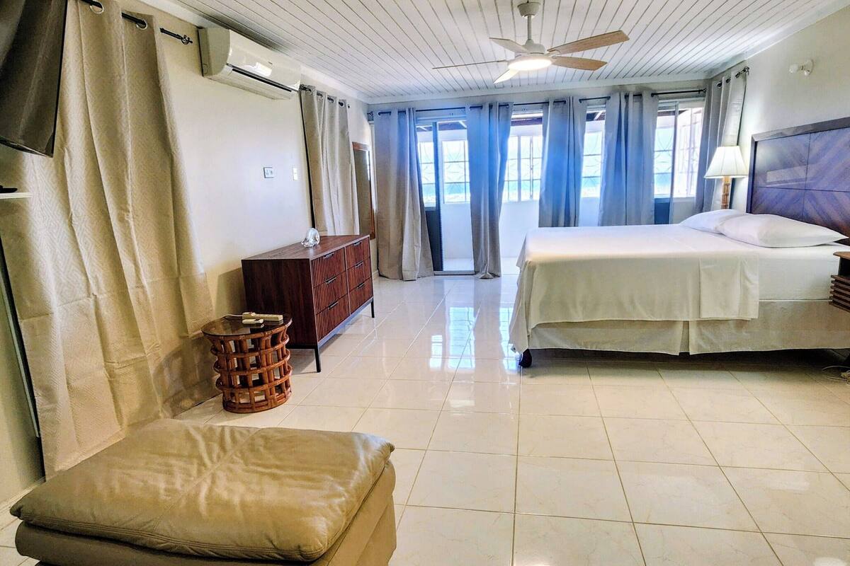 Une chambre d’hôtel comprenant un lit, un canapé, une petite table, une commode et un ventilateur de plafond.
