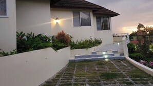 A modern house with a white exterior, a sloped roof, and a staircase leading to the entrance. - Comfy Villa With Ocean View (St. James Parish)