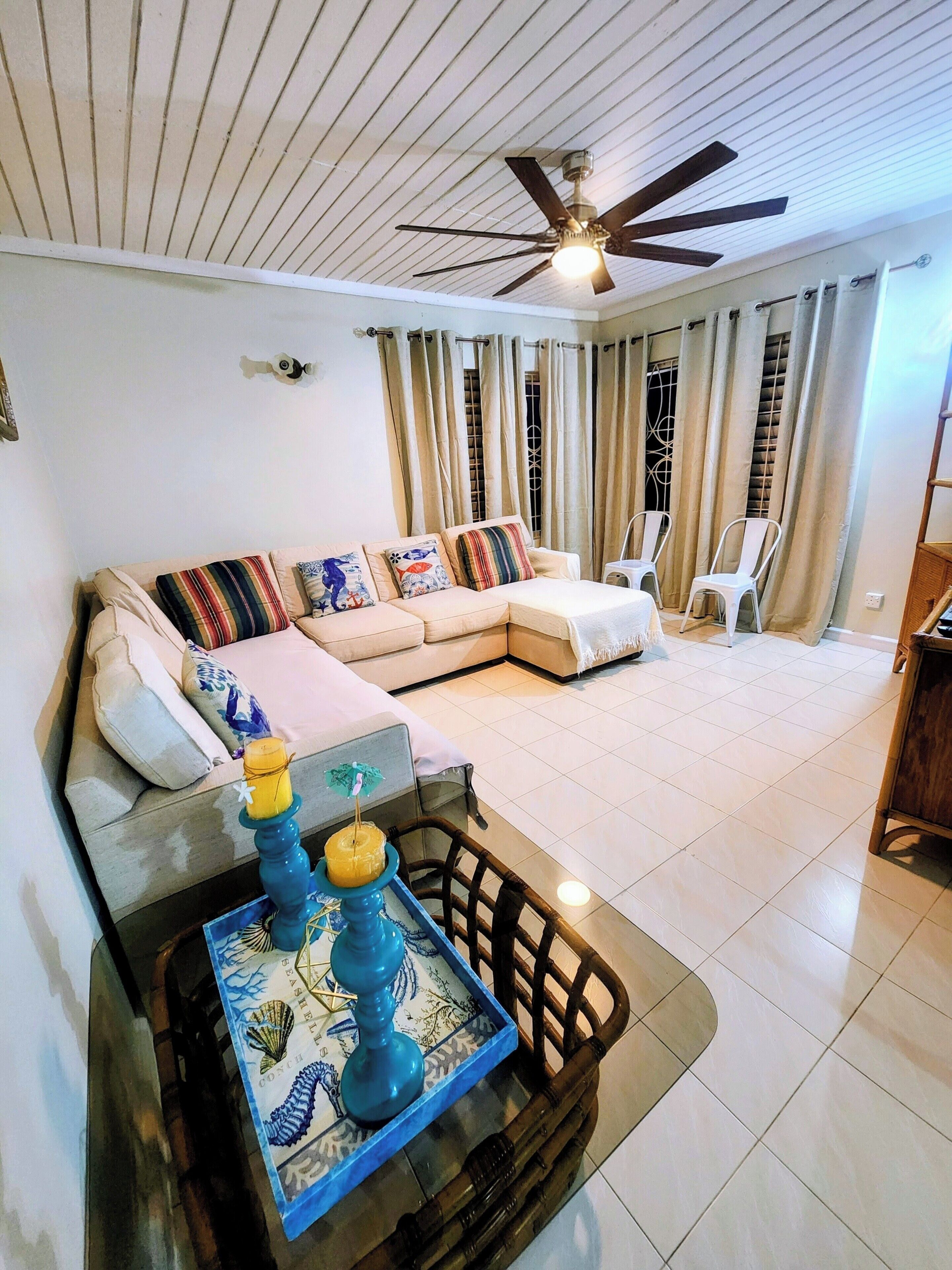 A living room with a sofa, a coffee table with decorative items, a ceiling fan, and curtains.
