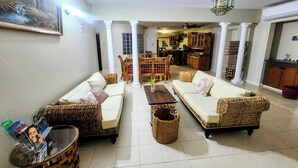 A spacious living area with two sofas, a coffee table, and a dining table with chairs. There is a kitchen in the background. - Comfy Villa With Ocean View (St. James Parish)