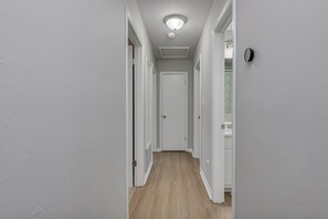 Ein enger Flur mit weißen Wänden und Holzböden, der zu einer geschlossenen Tür am Ende führt.