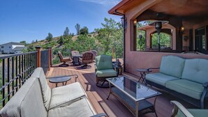 Um terraço com móveis de exterior, uma mesa de vidro e vista para uma paisagem montanhosa.