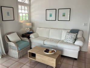 A living room with a white sofa, wicker chair, and a small wooden table with a bowl of fruit. - Island Time St John - Cinematic Views, 2 Beaches, Close to Town (Cruz Bay)