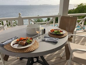 A round table with plates of food, a glass of wine, and a white bowl on a balcony overlooking the sea. - Island Time St John - Cinematic Views, 2 Beaches, Close to Town (Cruz Bay)