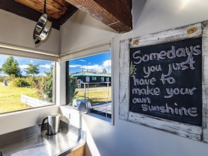 Une cuisine équipée d’une bouilloire, une fenêtre donnant sur un bâtiment verdoyant et un tableau noir sur lequel est inscrit un message inspirant.