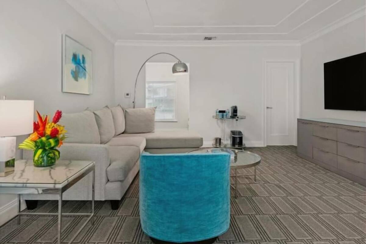 A modern living room with a sofa, a coffee table, a blue ottoman, a TV, and a painting on the wall.