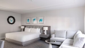 A modern hotel room with a large bed, a grey sofa, a small round table, and a wall-mounted mirror. - The Club at Birch House (Fort Lauderdale)
