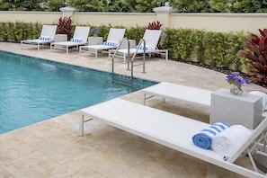 Zona de piscina con sillones de descanso, piscina y solárium con baldosas.