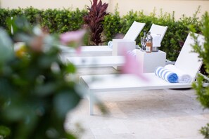 Sillones de exterior con toallas y botellas, rodeados de follaje.