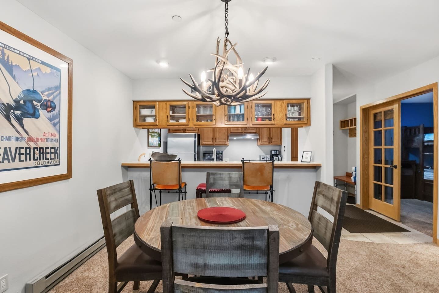 A dining area with a round table, chairs, a chandelier, wooden cabinets, and a framed picture on the wall.