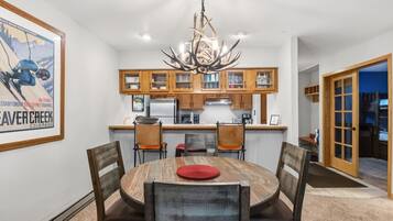 A dining area with a round table, chairs, a chandelier, wooden cabinets, and a framed picture on the wall.
