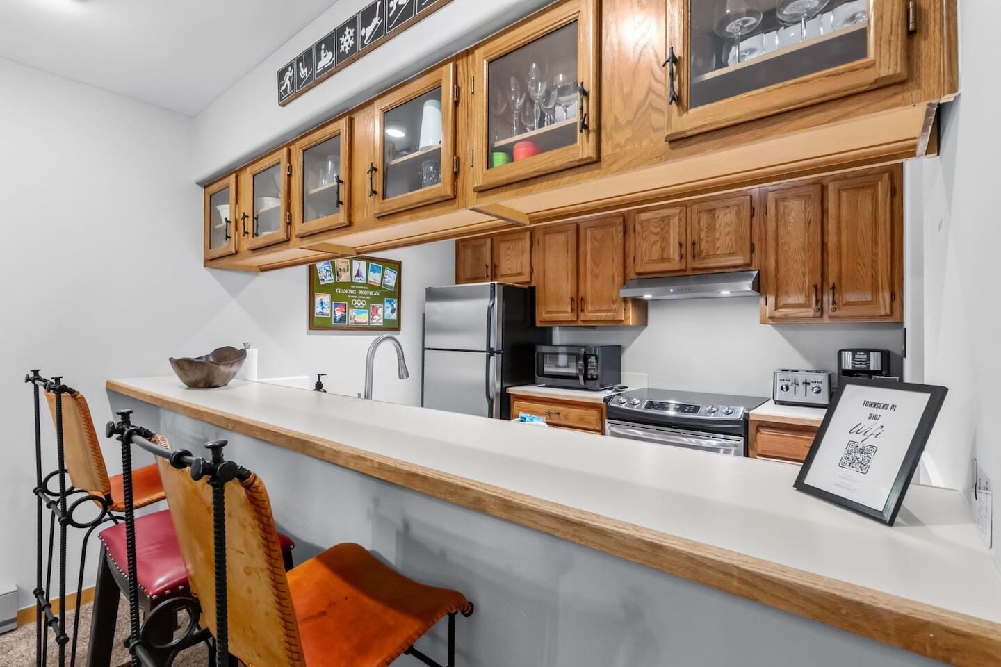 A kitchen with wooden cabinets, a stainless steel refrigerator, a microwave, an oven, and a sink.