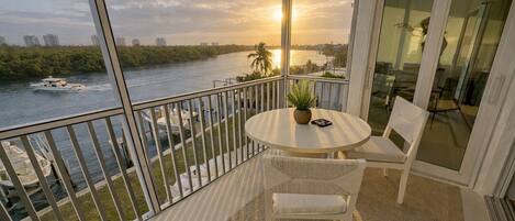Un balcon avec vue sur une rivière, un bateau et un coucher de soleil.