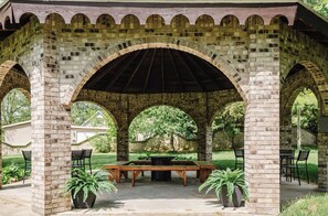 Um pavilhão ao ar livre com abóbadas de tijolo, uma mesa central e plantas em vasos.