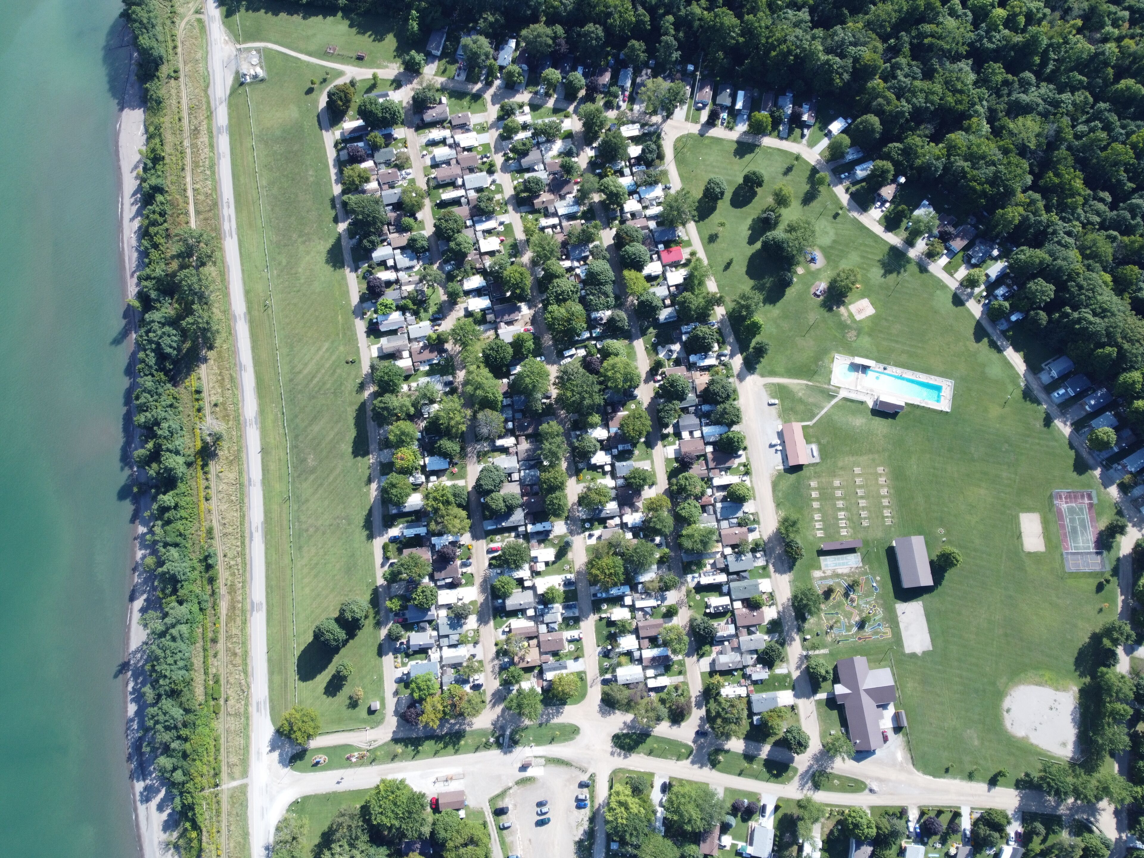 An aerial view of a residential area with houses, a swimming pool, and a tennis court.. Wildwood By The Lake! Cottage Rental in Private Park next to Lake Erie!