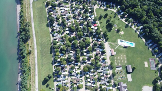 An aerial view of a residential area with houses, a swimming pool, and a tennis court. - Wildwood By The Lake! Cottage Rental in Private Park next to Lake Erie! (Morpeth)