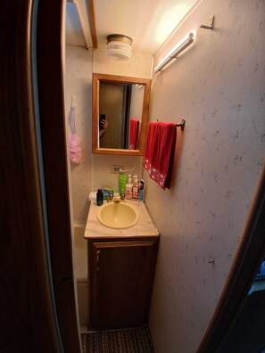 A compact bathroom with a wooden vanity, a mirror, a sink, and a red towel hanging on the wall.