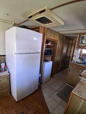 Eine kleine Küche mit einem weißen Kühlschrank, Holzschränken und einer Mikrowelle.