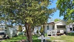 A mobile home park with several RVs and trailers, a tree-lined driveway, and a well-maintained lawn. - Wildwood By The Lake! Cottage Rental in Private Park next to Lake Erie! (Morpeth)