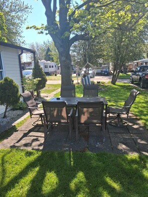 A patio with a table and chairs, surrounded by grass and trees.