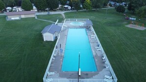 An aerial view of a rectangular swimming pool with a deck, surrounded by a grassy area and a small building. - Wildwood By The Lake! Cottage Rental in Private Park next to Lake Erie! (Morpeth)